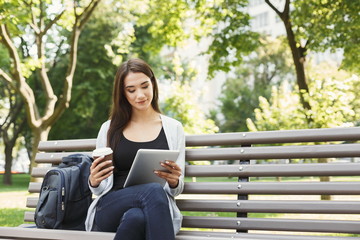 Obraz premium Smiling woman in park using digital tablet