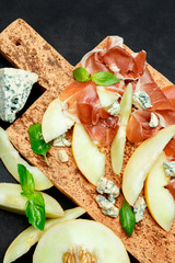 italian food with melon, prosciutto and cheese on cork cutting board
