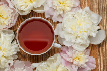 Flat lay over wooden background with peonies and cup of tea