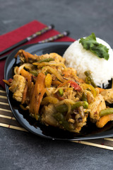 Fried vegetables with turkey meat and rice on the black plate. Asian delicates dishes with chili sauce.
