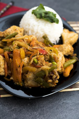 Fried vegetables with turkey meat and rice on the black plate. Asian delicates dishes with chili sauce.