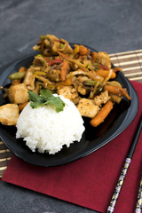 Fried vegetables with turkey meat and rice on the black plate. Asian delicates dishes with chili sauce.