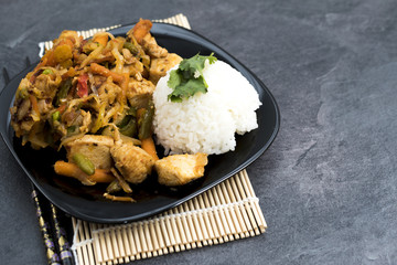 Fried vegetables with turkey meat and rice on the black plate. Asian delicates dishes with chili sauce.