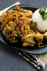 Fried vegetables with turkey meat and rice on the black plate. Asian delicates dishes with chili sauce.