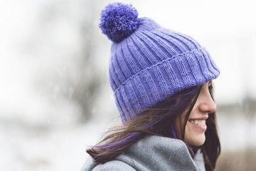 Young woman in modern knitted purple hat outdoors on snowy winter day. Closeup, natural light, no retouch.