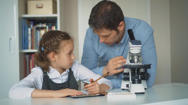 Little girl with teacher in science class with microscope on the table.