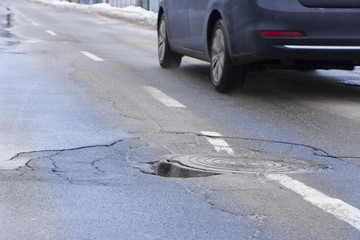 The car drives past the pothole with puddles on the road
