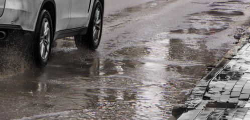 The car drives past the pothole with puddles on the road
