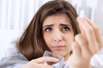 Sick young woman in bed looking pill medicine funny expression