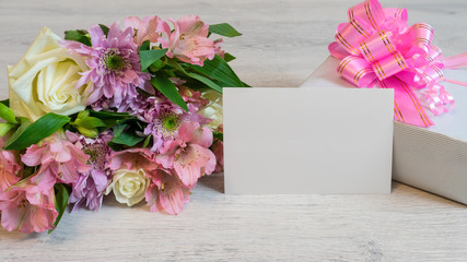 Colorful spring bouquet of rose, chrysanthemum and alstroemeria flowers with empty card and gift box on wooden background
