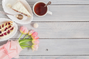 A cake with cherries, cup of tea and pink tulips on white wooden