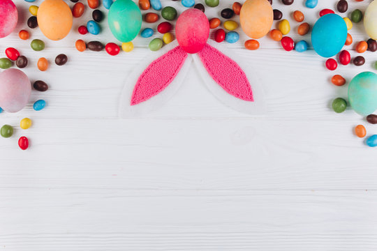 Wooden table to Easter around eggs, candy and ears of a rabbit. Top view and flat lay.