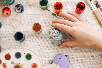 hand holding colored easter egg on rustic background with colorful paint. kids playing and coloring eggs, easter hunt concept. flat lay