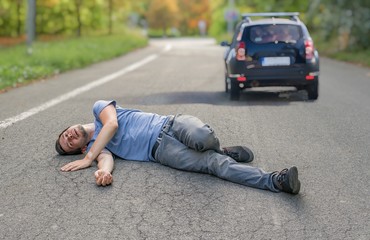 Hit and run concept. Injured man on road in front of a car.
