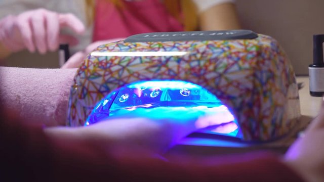 Female hand on the procedure of manicure. Drying the coating gel varnish in the led lfmpe. 4K