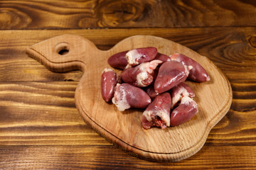 Raw chicken hearts on cutting board on wooden table