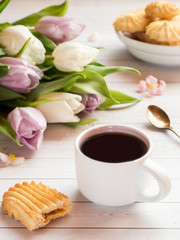 Coffee Cup with biscuits and tulips on a wooden table