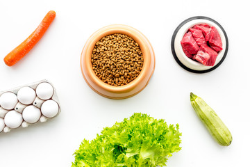 Dry pet food with natural ingredients. Raw meat, vegetables zucchini and carrot near eggs on white backgroud top view