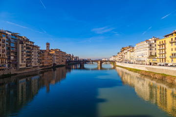Obraz premium Cityscape view on Arno river with famous Holy Trinity bridge in Florence. Reflections on water. Old colorful houses on the side. Tuscany, Italy