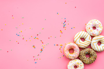 Donuts decorated icing and sprinkles on pink background top view copy space pattern