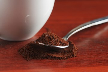 A spoon filled with ground coffee lies on a wooden table. Near the white cup. Close up view. Macro.