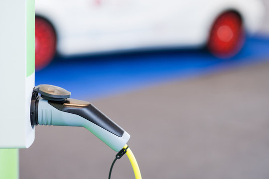 Electric car concept - closeup of the plug for charging on charge station with car in the background - selective focus with room for copy text.