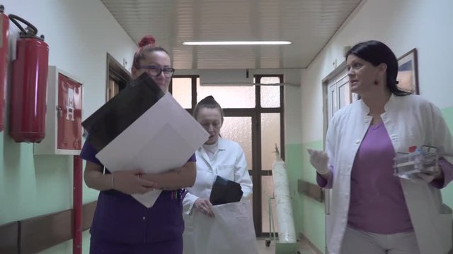 Nurses team with medical documentation and laboratory tubes together coming from hospital room and passing through hallway of ward, concept medicine, steadicam, tracking, gimbal shot, interior scene.
