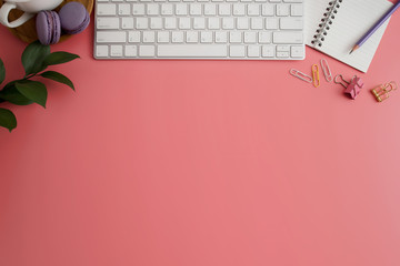 Styled stock photography pink office desk table with blank notebook, keyboard, macaroon, supplies and coffee cup. Top view with copy space. Flat lay.