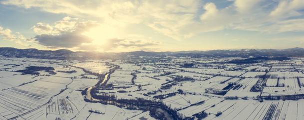 Aerial view of river flowing through snow covered countryside at sunset.