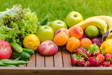 Various vegetables and fruits on a wooden tray against a background of green grass