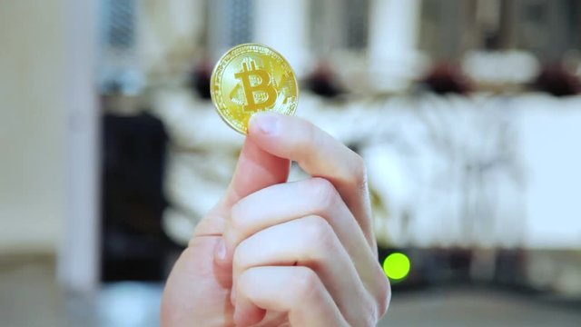 Crop shot of hand showing souvenir golden bitcoin working on mining farm.