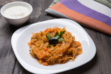 stewed cabbage in a white plate on a wooden table, sour cream and a towel