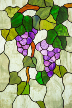 A stained glass panel depicts ripe purple grapes on a vine with green leaves.