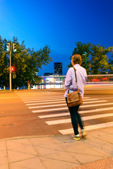 Young Woman Stands in Front of Crosswalk with Red Traffic Lights. Abstract Blur Long Exposure Night City Landmark.