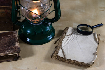 Old oil lamp and books lying on the table. A flame from an old source of light illuminating old prints.