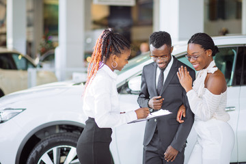 Beautiful young couple signs documents at dealership showroom.
