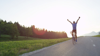 LENS FLARE: Ecstatic cyclist looking into the evening sky and outstretching arms