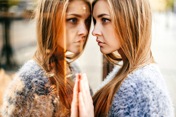 Self reflection portrait of amazing young girl in mirrored window. Unusual strange pretty woman...