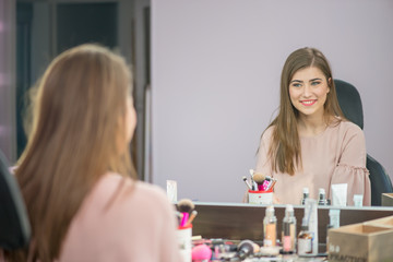 Beautiful woman with hairstyle and makeup looking at the mirror in beauty salon one