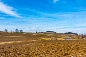 Straw bales and manure on the countryside field. Spring fields and preparation for agriculture. Typical czech countryside land, trees and blue sky