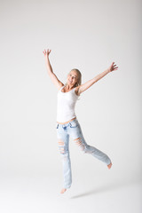 Fototapeta premium Young smiling woman in jeans and a jersey jumping against a gray background.