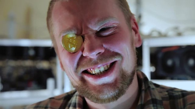 Young cheerful man with golden bitcoin instead of eyeglass posing excitedly at camera.