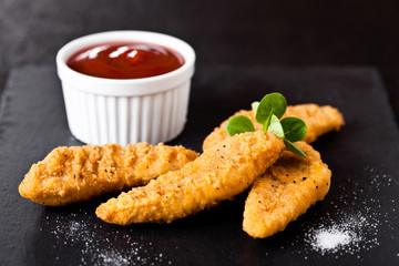 Fried chicken dippers on stone board with ketchup