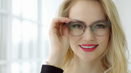 Close up of a young beautiful woman with glasses at the window and looking at camera.