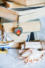 stack of old books, heart-shaped pendant, old scrolls, seashell - the concept of adventurers, travelers, dreamers and treasure hunt