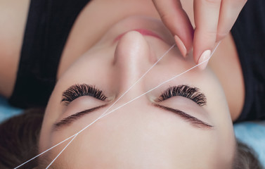 The make-up artist plucks her eyebrows with a thread close-up. Face care beauty treatments in the...