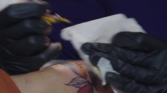 Professional master is painting tattoo with red ink, fills drawing with color. Works in black latex gloves with handmade rotor gun machine in studio. 4k