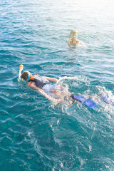 Two teenagers enjoying snorkeling in turquiose tropical sea. Girl swimming on sea surface and boy swimming and looking at camera.