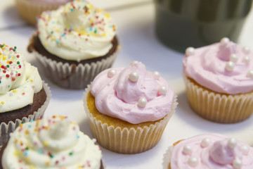 vanilla muffin with pink cream lies on a white wooden table on the background of other muffins