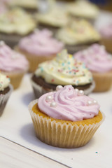 vanilla muffin with pink cream lies on a white wooden table on the background of other muffins